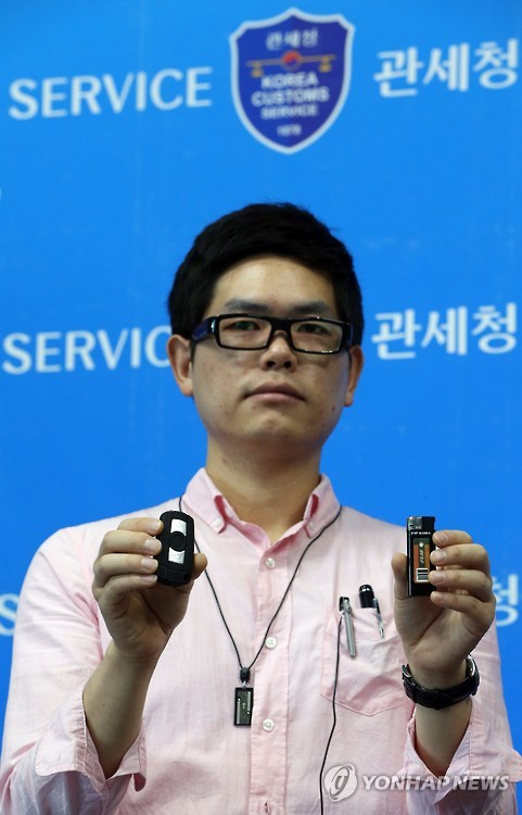Government official presenting various forms (glasses, necklace, lighter, car key, pen, tie pin) of miniature cameras.