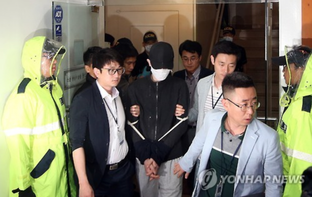 Flanked by police officers, the suspect behind the brutal murder of a 22-year-old woman exits the bathroom of a karaoke bar near a subway station in Seoul's upscale Gangnam district on May 24, 2016, after staging a reenactment. (image: Yonhap)