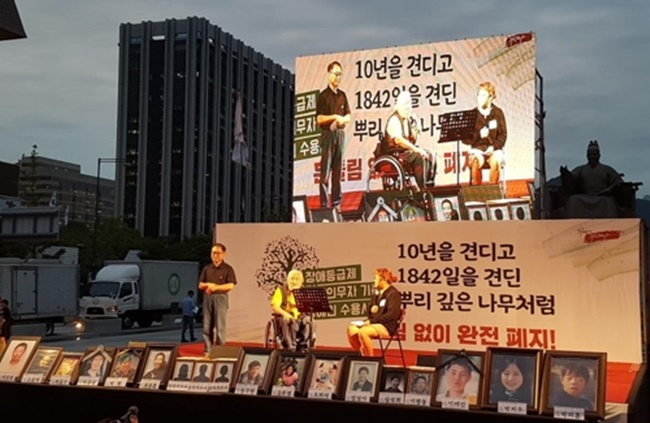 A group of disability activists cheered on their achievement after 1,842 days of protest, to be exact, at the heart of the South Korean capital on Tuesday, as the Ministry of Health and Welfare agreed to gradually do away with the controversial requirements that have made it extremely hard for those with financial supporters to claim disability benefits despite not receiving any actual help. (Image: Yonhap)