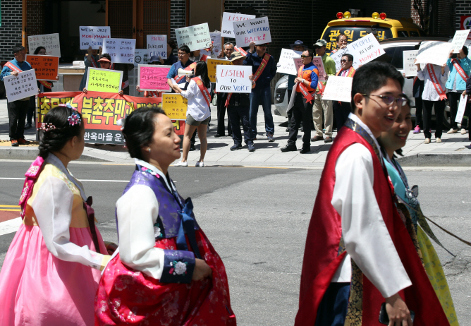 Tourists wearing traditional Korean attire, or "hanbok," pass by a group protesting against tourist visits to Bukchon Hanok Village in central Seoul. The residents from the traditional village argue that an overwhelming number of visitors disrupts their lives and leaves tons of trash in the neighborhood. (image: Yonhap)