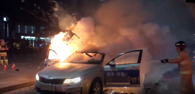 A taxi being engulfed in a blaze while firefighters approach the scene to put out the fire. (image: Seoul Jongno Fire Station)