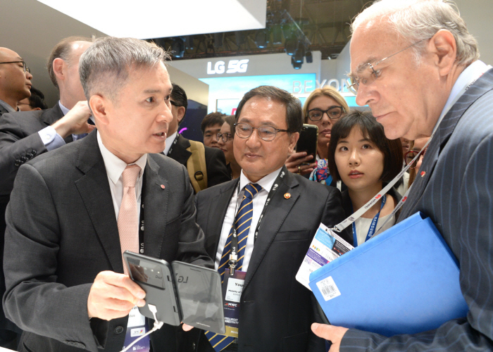 Ha Hyun-hoi (L), CEO of LG Uplus Corp., shows a mobile application on a LG V50 ThinQ smartphone to visitors at its booth at MWC Barcelona on Feb. 25, 2019. (Yonhap)