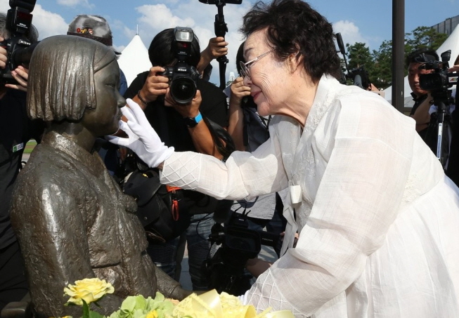 Lee Yong-su, a survivor of sex slavery perpetrated by the Japanese military during World War II, runs her hands over the face of a girl statue that represents all victims of Tokyo's crime against humanity at a ceremony in Seongnam, south of Seoul, on Aug. 13, 2019. (Yonhap)