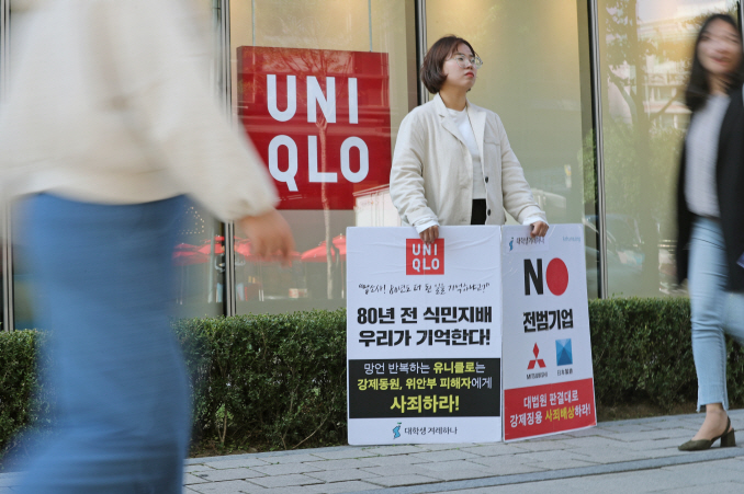 A university student stands with banners criticizing Uniqlo's controversial TV advertisement in front of a Uniqlo store in Seoul on Oct. 22, 2019. (Yonhap)