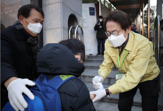 Cho Hee-yeon (R), the superintendent of the Seoul Metropolitan Office of Education, sprays sanitizer on a student's hands at Bongeun Elementary School in southern Seoul on Feb. 3, 2020. (Yonhap)