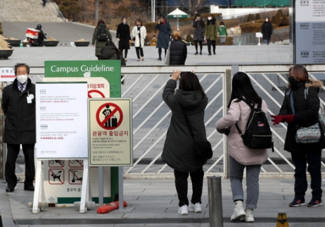 Foreign tourists take photos in front of the entrance of Ewha Womans University in Seoul on Feb. 7, 2020, as the school restricts their visits amid the escalating coronavirus crisis. (Yonhap)