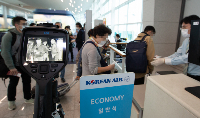 This photo taken on March 5, 2020, and provided by Korean Air shows a company employee checking the temperature of outbound passengers at a boarding gate at Incheon International Airport in Incheon, western Seoul.