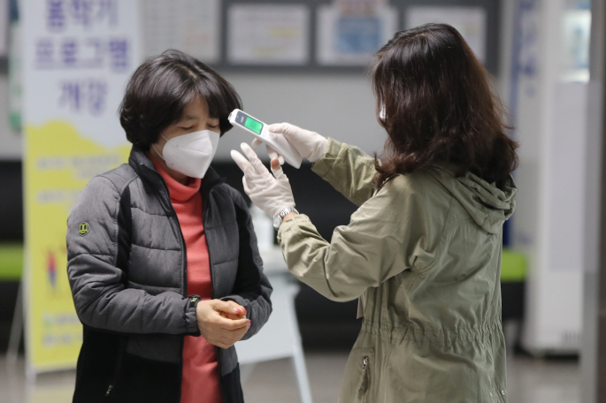 An election official checks the body temperature of a voter at a polling station for the parliamentary elections in Gwangju, 330 kilometers south of Seoul, on April 15, 2020. (Yonhap)