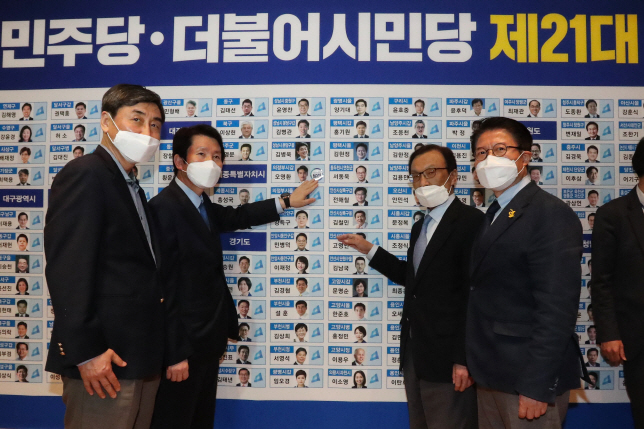 This photo, taken on April 15, 2020, shows officials at the Democratic Party and its satellite party posing in front of a board at the National Assembly in Seoul showing seats the parties have secured in the general elections. (Yonhap)
