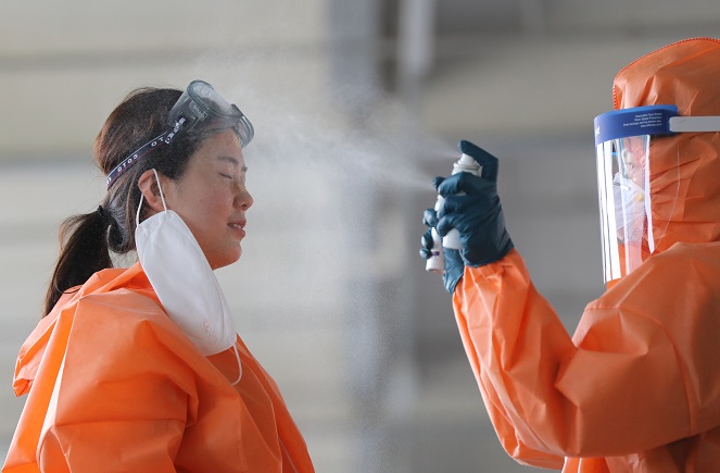 A medical worker in protective gear sprays face mist on her colleague at an outdoor clinic for coronavirus tests inside a public health facility in the southwestern city of Gwangju on June 5, 2020, to counter the scorching heat amid a heat wave hitting the region. (Yonhap)