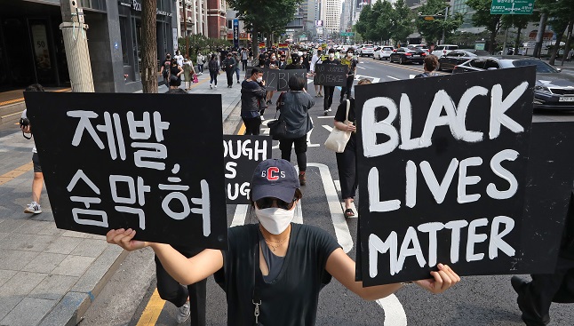Clad in black, a person marches in central Seoul on June 6, 2020, holding pickets reading "Black Lives Matter" and "Please, I Can't Breathe."(Yonhap)