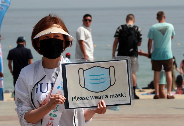 An official in the southeastern port city of Busan holds a sign that asks visitors to wear masks at the city's Haeundae Beach on July 5, 2020. (Yonhap)