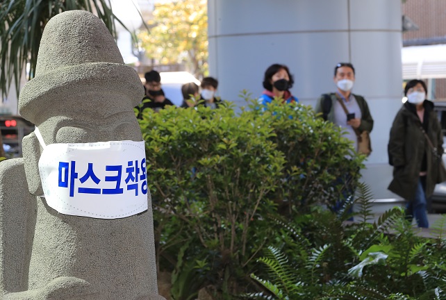 This file photo shows a stone mascot of Jeju Island wearing a mask as tourists pass by. (Yonhap)