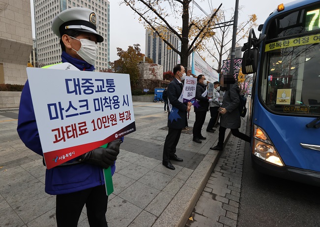 Seoul city and bus officials hold up signs on a new 100,000 won fine for people not wearing a face mask in public, at a bus stop in Gwanghwamun, downtown Seoul, on Nov. 13, 2020. (Yonhap)