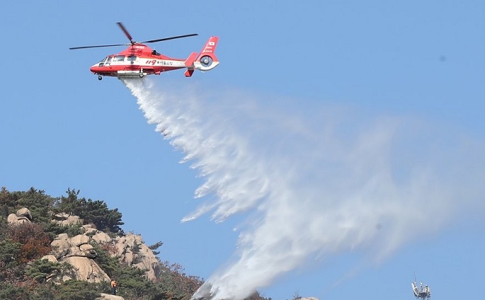 A helicopter of the state-run forest service dumps water on a fire on Mount Bukhan in Seoul's Eunpyeong Ward on Oct. 30, 2020. (Yonhap)
