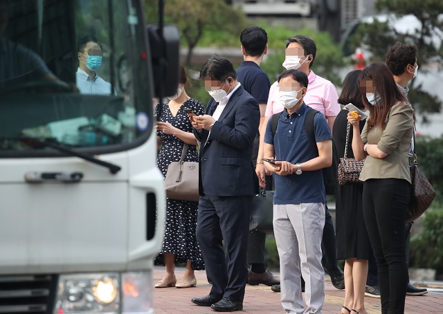 This June 15, 2020, file photo shows people checking their phones at a bus stop in central Seoul amid the new coronavirus pandemic. (Yonhap)