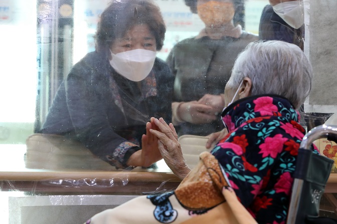 A patient (R) on one side of a transparent screen due to preventative measures against COVID-19 meets with a family member at a senior care hospital in Gwangju, 330 kilometers south of Seoul, on March 9, 2021. (Yonhap)