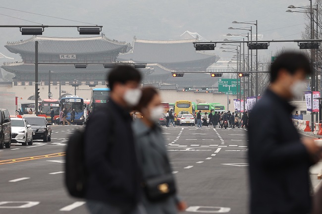 Masked people walk across a street near Gwanghwamun Square in downtown Seoul on March 12, 2021. (Yonhap)