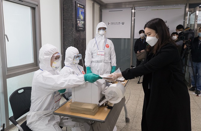 This photo taken on March 23, 2021, shows Seoul Metropolitan Government officials providing a sample ballot to a woman in a straw vote held at Seoul Youth Hostel in central Seoul ahead of the city's mayoral election on April 7. (Yonhap)