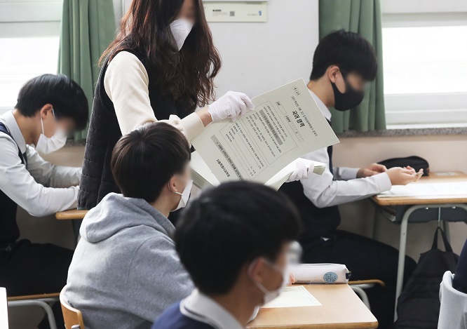 This photo taken on March 25, 2021, shows a teacher wearing a mask and gloves handing out examination papers to students at a high school in Suwon, just south of Seoul, amid the COVID-19 pandemic. (Yonhap)