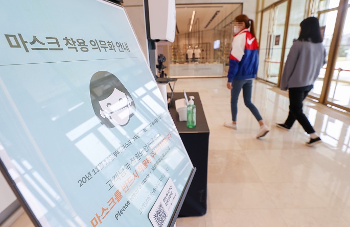 Customers pass by a signboard on a mask mandate at the entrance of a department store in Seoul on April 11, 2021. (Yonhap)