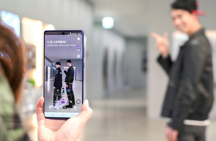 A model takes a photo with a digital version of "League of Legends" professional gamer Lee Sang-hyeok on SK Telecom Co.'s Jump AR app, in this photo provided by the company on April 12, 2021.