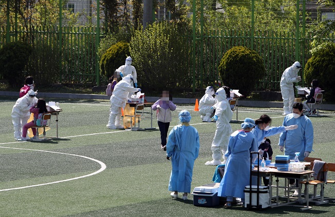 Health workers clad in protective suits collect samples from students and teachers at a makeshift virus testing clinic at an elementary school in Gwangju on April 19, 2021. (Yonhap)