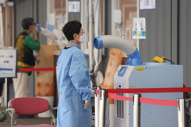 A medical worker takes a short break in front of a cool air system at a makeshift COVID-19 testing site in central Seoul on June 20, 2021. (Yonhap)
