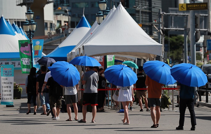 Citizens, holding umbrellas amid a heatwave, wait in line to receive coronavirus tests at a makeshift clinic in front of Seoul Station on July 18, 2021. (Yonhap)