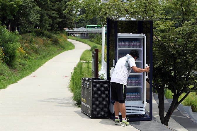 A person takes a bottle of water from a refrigerator set up for villagers at a neighborhood park in Seoul amid a heat wave on July 20, 2021. Such fridges, which are installed in various places, will provide free water until the end of August. (Yonhap)