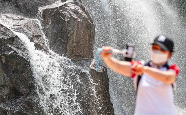 A citizen tries to beat the scorching heat wave at an artificial waterfall in eastern Seoul on July 24, 2021. (Yonhap)