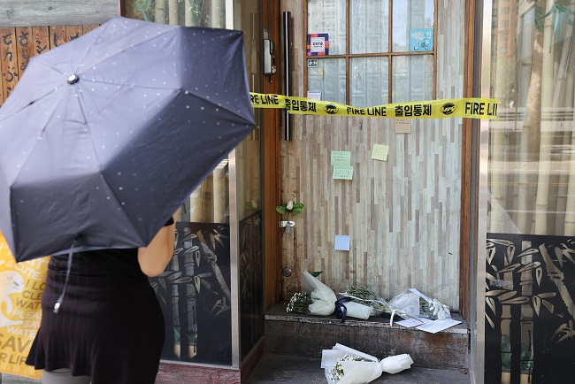A person looks at memos and chrysanthemums placed in front of a beer hall in Seoul on Sept. 14, 2021, after its owner apparently took his own life a week earlier due to COVID-19-related business difficulties. (Yonhap)