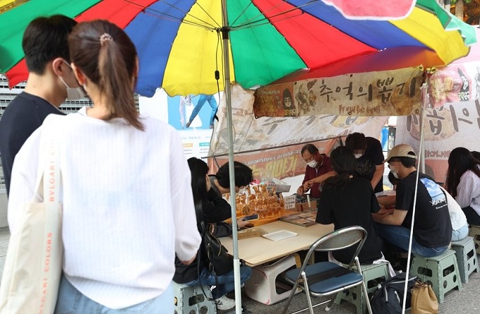 People enjoy "dalgona bbobggi" by a street vendor in Seoul on Sept. 30, 2021, as the nostalgic Korean game is rapidly gaining popularity around the world thanks to mega-hit Netflix series "Squid Game." Dalgona is simply made of sugar and baking soda. (Yonhap)