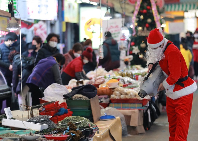 Wearing a Santa Claus outfit, an official from the local office of the SMEs and Startups disinfects a traditional market in the southeastern port city of Busan on Dec. 20, 2021, as part of efforts to support self-employed workers and small merchants hit by slack business amid the coronavirus pandemic. (Yonhap)