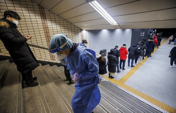 A medical worker climbs the stairs in front of a crowded COVID-19 testing station in Seoul's eastern district of Songpa on Dec. 17, 2021. Seoul's morning low on this day recorded minus 5 C. (Yonhap)