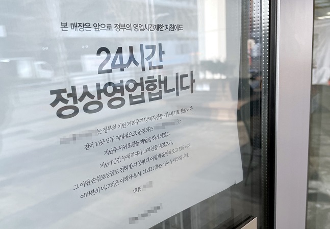 A notice is placed in front of a cafe in Incheon, 40 kilometers west of Seoul, on Dec. 21, 2021, announcing its plans to remain open 24 hours in defiance of government-mandated COVID-19 business curfews. (Yonhap) 