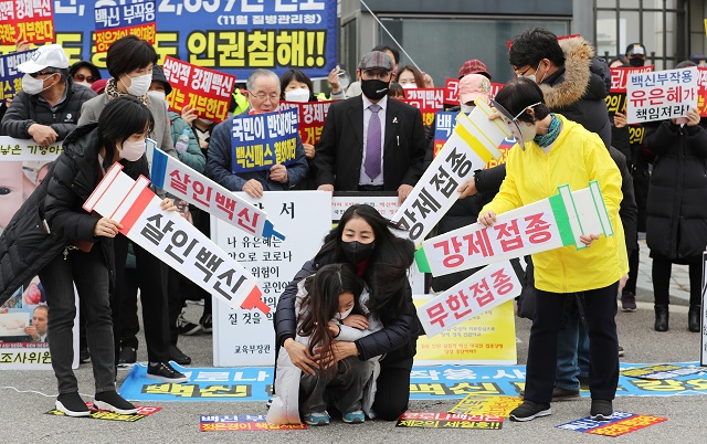A parent holds her child as part of a rally at the government complex in Sejong, central South Korea, on Dec. 9, 2021, to demand the government withdraw its plan to expand the COVID-19 vaccine pass system to teenagers. The system requires them to present COVID-19 vaccination or negative test certificates at multiuse facilities, including public study rooms and cram schools, a measure that critics say amounts to forcing people to get vaccinated. (Yonhap)