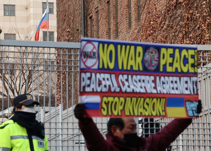 A man holds a banner that says, "No War Peace, Stop Invasion," in front of the Russian Embassy in Seoul on Feb. 25, 2022, to oppose Russia's invasion of Ukraine. (Yonhap)