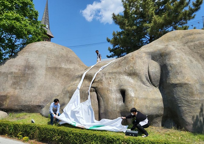 Municipal workers take a mask off a statue of a primitive man in Dalseo Ward of the southeastern city of Daegu on May 2, 2022, as the country allowed people to not wear masks outside starting the same day amid a decreasing trend in the number of daily COVID-19 cases, in this photo released by the ward office. The office placed the mask on the 20-meter-long and 6-meter-high structure on May 15, 2020, to encourage people to wear masks amid a surge in the number of coronavirus infections.