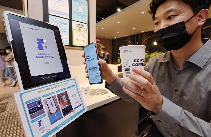 An environment ministry official demonstrates the disposable cup deposit system at a cafe in Seoul on May 6, 2022. (Pool photo) (Yonhap)