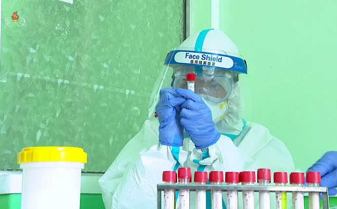In this photo from the North's Korean Central Television on May 20, 2022, a medical worker wearing protective gears looks at a specimen container of a COVID-19 test swab. (Yonhap)