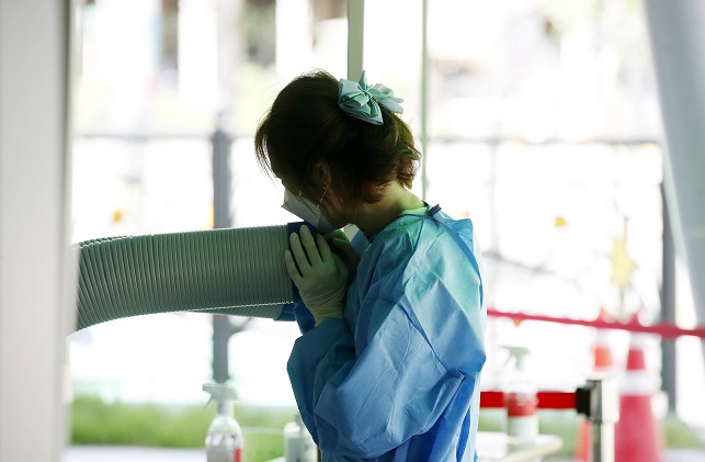 A medical worker takes a break in front of an air cooler at a COVID-19 testing station in Gwangju, 268 kilometers south of Seoul, amid a heat wave on July 29, 2022, in this photo provided by a local ward office.