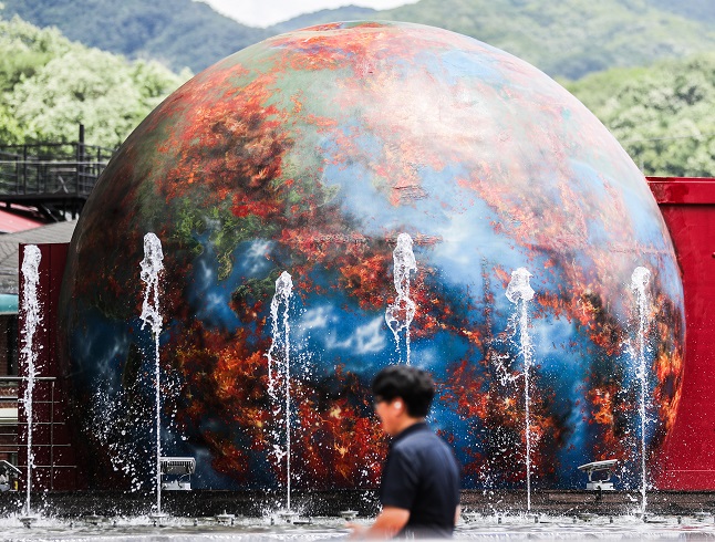 A man walks past an installation featuring a burning Earth at a park in Daegu, 237 kilometers southeast of Seoul, on July 5, 2023. (Yonhap)