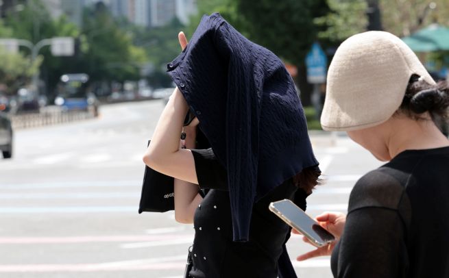As scorching temperatures gripped the nation on July 1, with heat wave warnings issued across most regions, a Seoul resident shields themselves from the sun with clothing while walking through Gwanghwamun Intersection. (Yonhap)