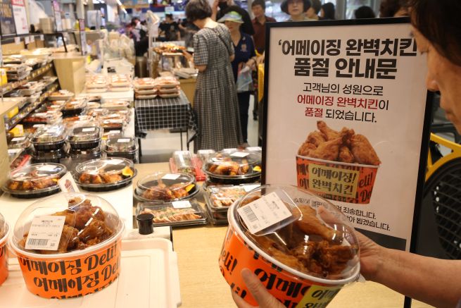 On July 6, a shopper exchanges a numbered ticket for fried chicken at an E-Mart store in Seoul. The retailer drew strong consumer response by offering its “Amazing Perfect Chicken,” made with 100 percent domestically sourced fresh chicken, for 3,480 won (one per customer) through that day. (Yonhap)