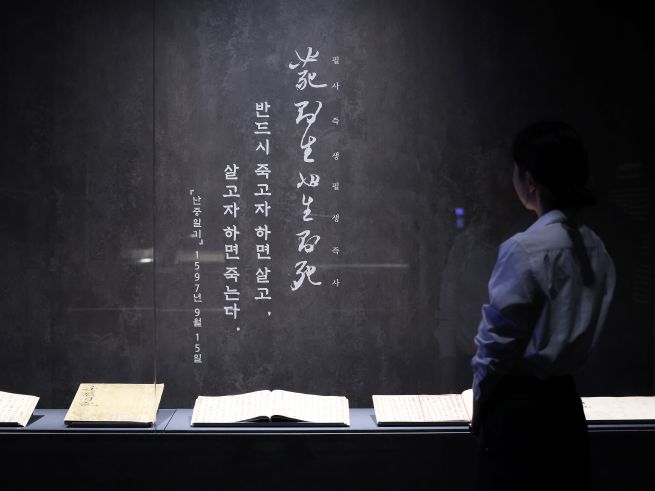 At the media preview for the exhibition “Our Admiral Yi Sun-sin” held at the National Museum of Korea in Yongsan, Seoul, on Nov. 27, a visitor looks at original manuscripts of the Nanjung Ilgi (War Diary) and related artifacts. The exhibition, organized to mark the 480th anniversary of Admiral Yi’s birth and the 80th anniversary of Korea’s liberation, will be open to the public free of charge through Dec. 4. A panel displays one of Yi’s famous maxims: “Those who are determined to die will live, and those who wish to live will die.” (Yonhap)